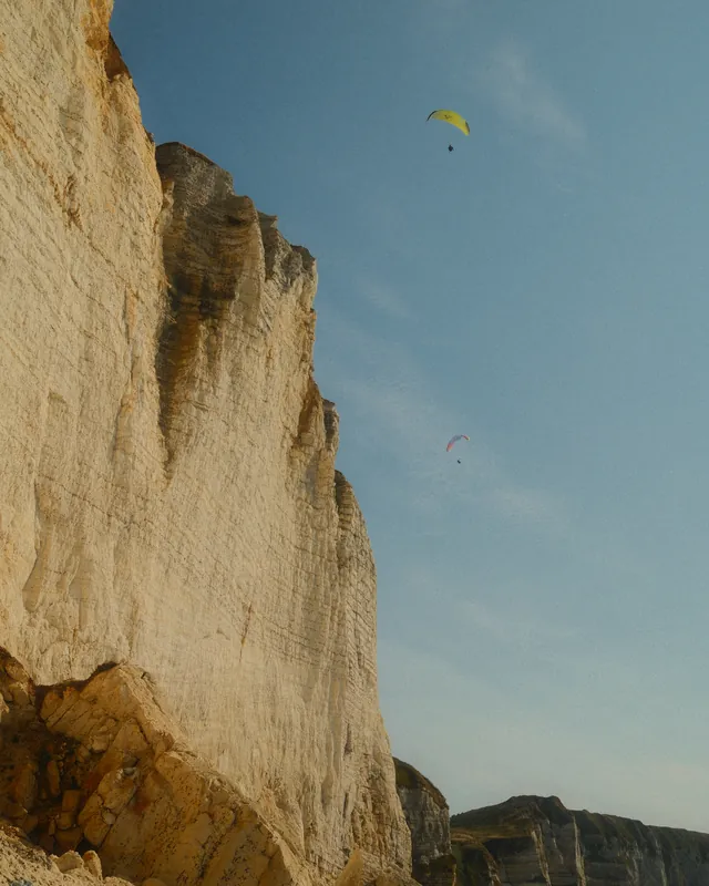 Two paragliders over tall white chalk cliffs, seen from the beach below